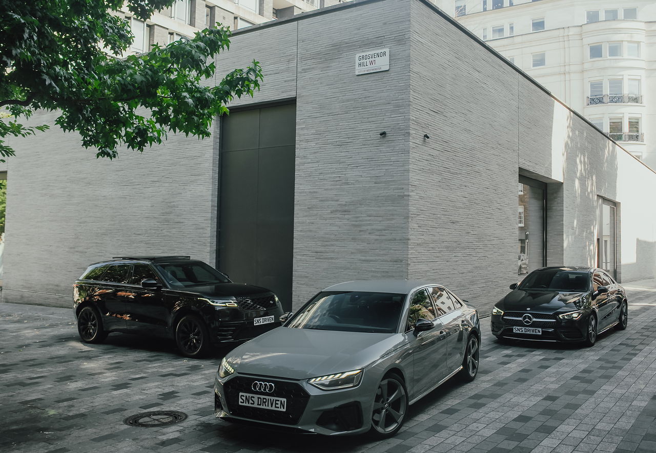 Three SNS vehicles — a Range Rover Velar, Audi A4 and Mercedes CLA — parked outside a stone building on Grosvenor Hill, W1